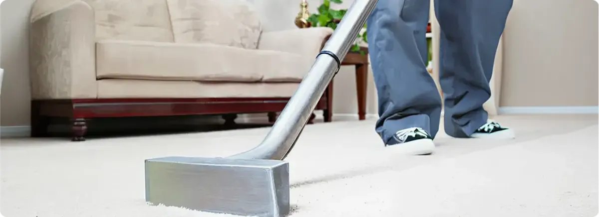 Carpet cleaning technician using a hot-water extraction wand on a light-colored carpet in a living room, Birmingham, AL.